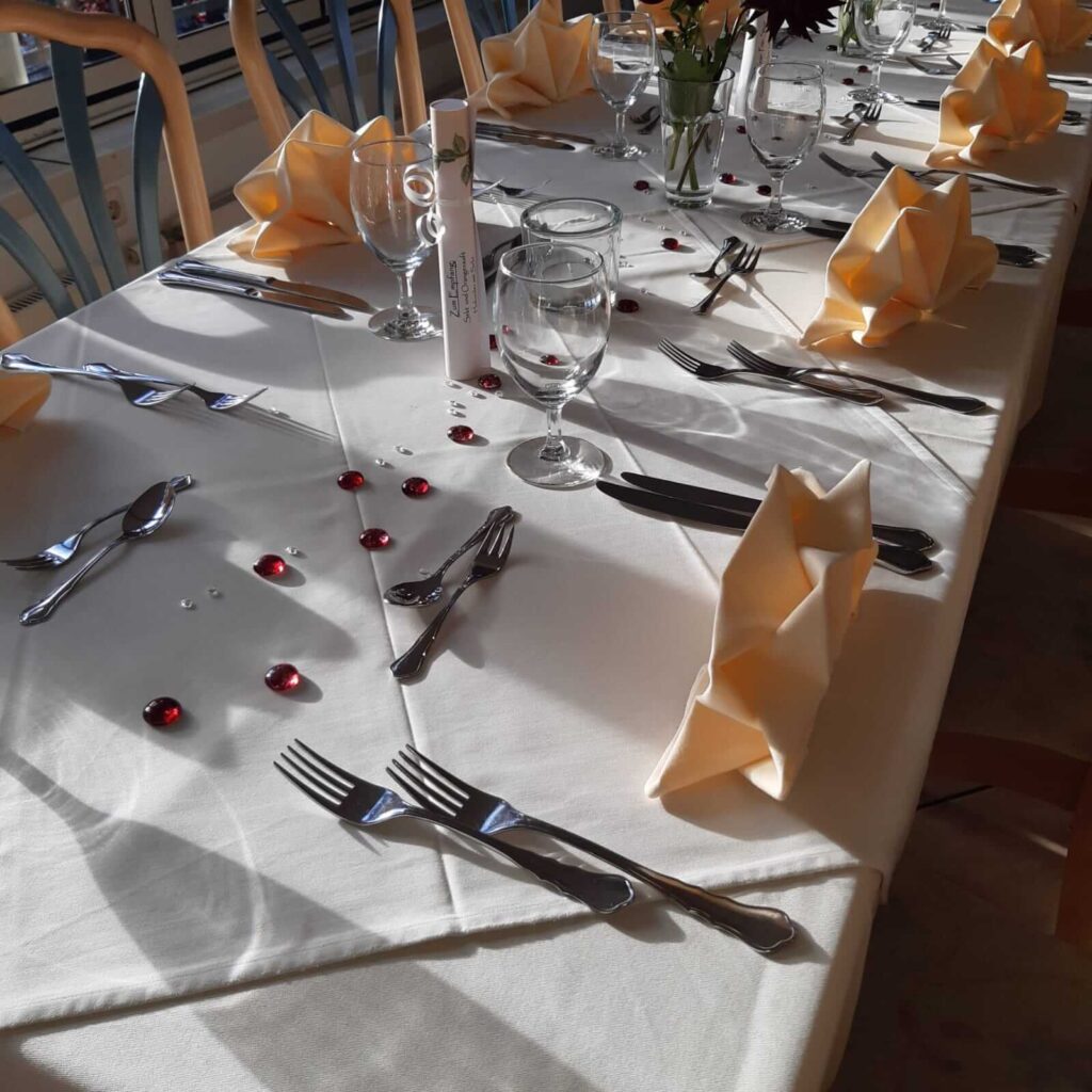 Bild einer Rose, diese steht auf einem Tisch in einer Vase, die Rose ist Rot. besteck liegt ebenfalls auf dem Tisch.
